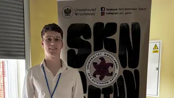 Zdjęcie Studenta Naszego Wydziału - Macieja Dysierowicza na tle baneru SKN GATUN z Uniwersytetu Wrocławskiego
