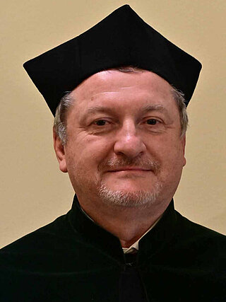 Oficjalna fotografia portretowa dr. hab. inż. Jana Ziai, profesora uczelni, Prodziekana ds. Nauki i Współpracy Wydziału Wiertnictwa, Nafty i Gazu AGH. Sylwetka ujęta od pasa w górę, w czarnej todze akademickiej z biretem, na jednolitym jasnym tle studyjnym.