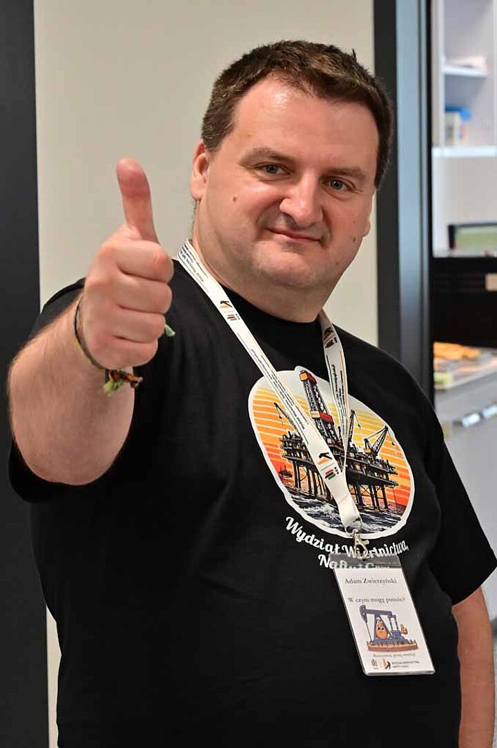 Doktor Adam Zwierzyński z Wydziału Wiertnictwa, Nafty i Gazu zaprasza na studia trzymając uniesiony kciuk do góry na wyciągnietej w kierunku obserwatora ręce